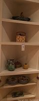 Shelves holding assorted unmarked French and majolica ceramics including a basket, vase, fruit containers, and other decorative items.