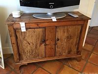 Front view showing wooden entertainment center TV stand with two cabinet doors, turned knob handles, bracket feet, top surface wear