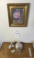 Overview of framed painting on wall with shelf containing porcelain figurine, floral trinket box, glass jar, and compact