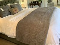 Wide shot of bed with white comforter, gray quilted runner and pillows