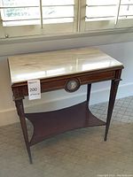 Front view of table showing marble top, carved wood legs, lower shelf and central medallion