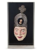 Front view of mask and metal headpiece in acrylic case against black backing
