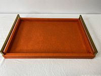 Full view of rectangular orange leather tray with brass handles showing raised sides and flat base