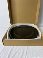 8 black charger plates stacked inside a cardboard box with white protective padding.