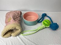 Dog accessories bundle showing small pink jacket, round food/water dish, and two chew toys with green and blue colors