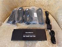 Front view of KVM switch main unit with cables and accessories arranged around it on a patterned fabric surface.