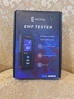 Front photo of Erickhill EMF Tester retail box, showing product image and three key features: color screen display, sound and light alarm, and data app.