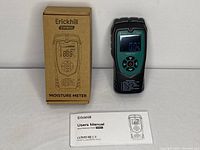 Front view of Erickhill EWM04 moisture meter device powered on showing digital display, alongside its original box and user manual laid flat.