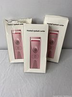 Three boxed pink heated eyelash curlers displayed upright with text 'Heated eyelash curler' on the boxes