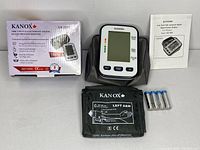 Complete lot laid out: digital blood pressure monitor, black adjustable cuff for left arm, four AA batteries, all placed next to product box and instruction manual.