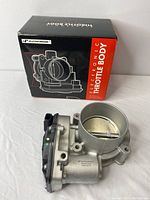 Photo of the electronic throttle body alongside its black and red box labeled 'Electronic Throttle Body Premium'. Shows the full side and top view of the throttle body with butterfly valve and connector visible.