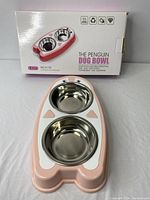 Photo of the packaging box showing product branding, features and the penguin-shaped dog bowl with stainless steel bowls on top.