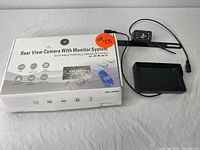 Photo of the rear view camera system box, monitor screen, and rear camera with cables.