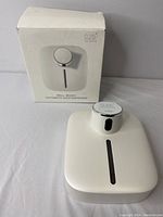 White automatic soap dispenser and its original packaging box on table surface, showing front and top details.