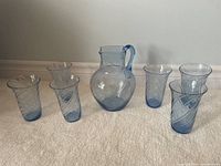 Full set of blue glass pitcher and six matching glasses displayed on floor
