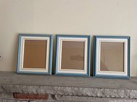 Three blue picture frames with white mattes arranged side by side on a stone ledge against a wall