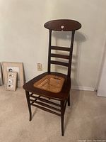 Full view of the antique chair showing the wooden frame, oval backrest, horizontal slats, and broken wicker seat.