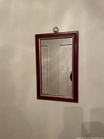 Front view of rectangular mirror showing red wood frame with gold inner trim and hanging ring at top.