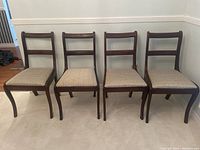 Front view of all four wooden dining chairs in a row showing curved legs and patterned seats.