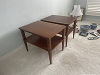 Pair of solid wood end tables placed side by side on a carpeted floor, showing the difference in wood tone between the two tables.