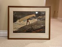 Framed print showing the full image of man with canoe and wooden frame on carpeted floor