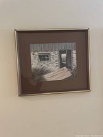 Framed watercolor painting showing an old rustic door and window set in textured stone walls, muted colors, with a brown matte and gold-frame