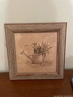 Front view of the framed picture showing the watering can with flowers and bee artwork.