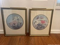 Two framed floral prints leaning against a wall, showing full view of both artworks and frames.