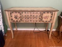 Frontal view of the painted wood table showing drawers and cupboard doors with decorative fruit paintings and checkered borders.