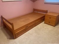 Twin/single pine bed frame with two large rolling drawers underneath and pink walls background