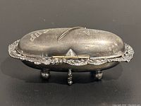 Angled side view of the antique silver plated oval trinket box showing the hinged lid and three ball feet.