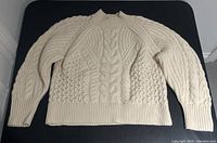 Full front view of cream cable knit sweater laid flat on black surface