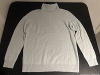 Full front view of pale blue turtleneck cashmere sweater laid flat.