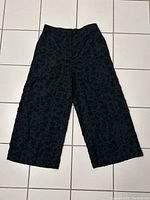Front view of black culotte style pants showing the wide legs and front texture details.