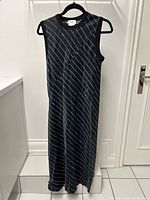 Full view of the black sleeveless DKNY dress with diagonal white stripes hanging on black hanger against white door and walls.