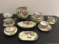 Photo showing the full lot of Victorian floral china pieces with violet designs arranged together, including cups, saucers, plates, and serving vessels.
