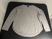 Grey Aqua Cashmere women's sweater laid flat on a black surface, showing the full front view with crew neck, long sleeves, and curved hemline