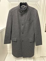 Full front view of buttoned dark grey overcoat against white background