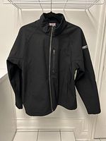 Front view of black Karbon jacket hanging on hanger showing full zipper, collar, and arm design.