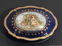 Top view showing the cobalt blue lid with gold trim and oval romantic scene details.