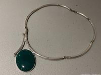 Full view of the silver tone necklace laid flat, showing the green stone pendant and tubular necklace segments.