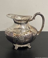 Front view of silver plated water pitcher showcasing hand chased floral pattern and curved handle