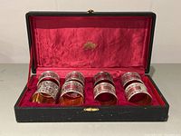 Box open showing full set of eight silver plated napkin rings with embossed coat of arms design, red lined interior.