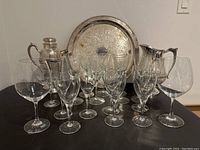 Full view of the set including silver plated tray, pitcher, cocktail shaker without spout cover, and 13 clear wine glasses of varying sizes.