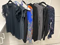 Lot of 10 women's blouses and sweaters hanging on rack showing colors and styles
