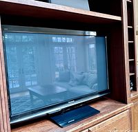 Full front view of Panasonic plasma TV set placed in wooden entertainment center showing screen and black bezel.