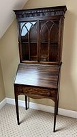 Front view of the entire two-part secretary desk showing the dark mahogany finish, tapered legs, drop front writing surface, upper cabinet with mullion detailed glass door, and Jacobean cornice.