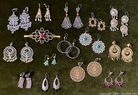 Full view of all earrings and hair clasp laid out on black background showing variety of styles and metal finishes.