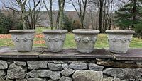 Four concrete planters displayed outdoors on a stone wall, showing the full set and relative size.