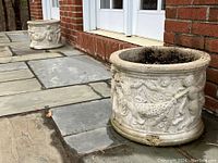 Photo showing the closer view of one concrete planter with cherub and animal relief, lipped rim, some damage and dirt inside.